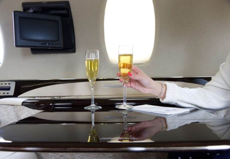 A person holding a champagne glass on a private jet, with another glass on the table next to them.