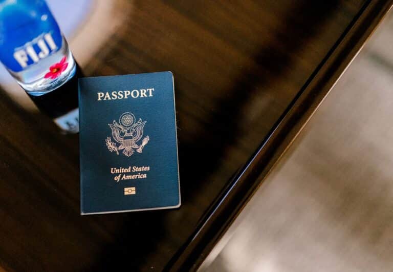 A United States passport on a wooden surface next to a bottle of Fiji water.