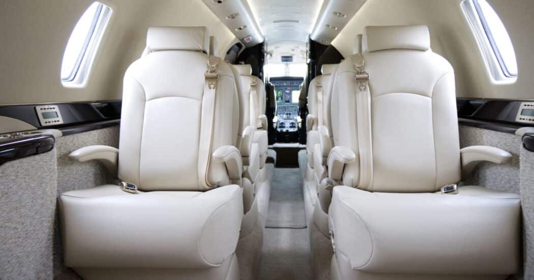 Interior of a private jet with cream-colored leather seats and a view of the cockpit at the front.