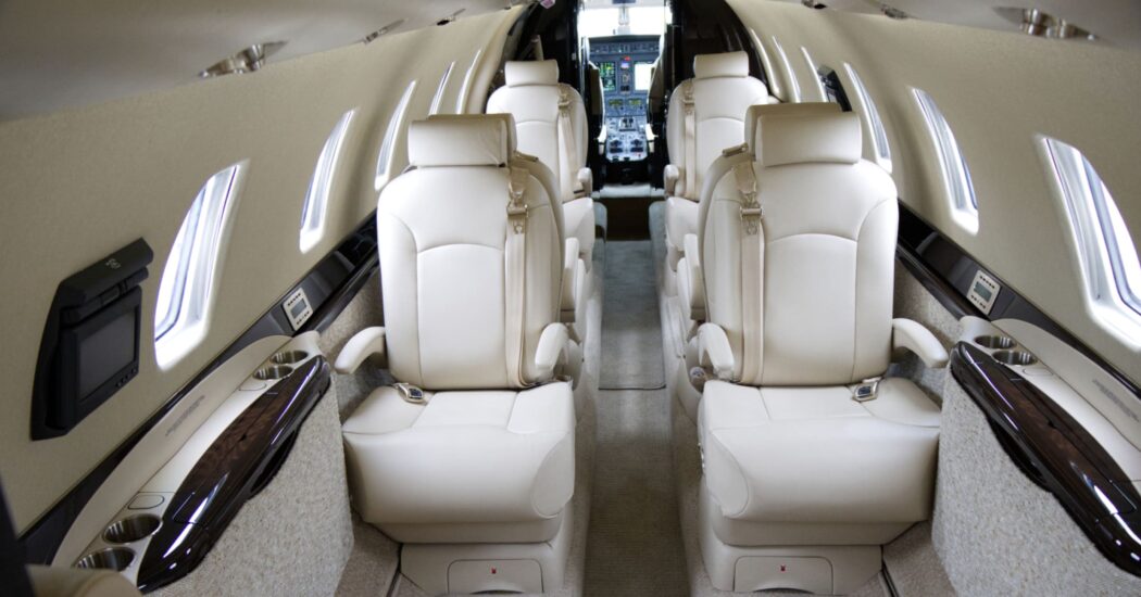 Interior of a luxurious private jet with beige leather seats and sleek design, leading to the cockpit in the background.