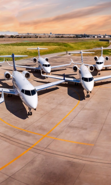 Four white and blue jets parked on an airport tarmac under a colorful sky.