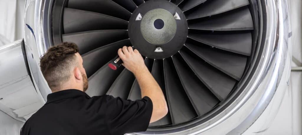 Person inspecting a jet engine with a flashlight in a hangar.