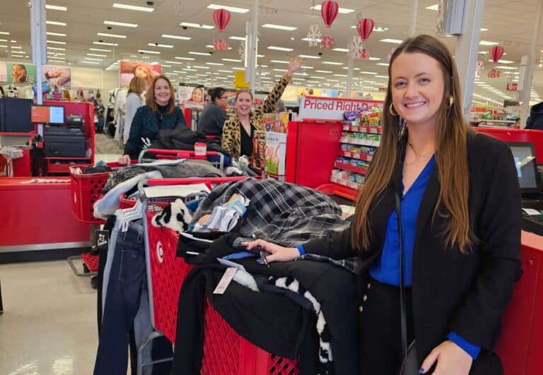 Women smiling with shopping carts full of clothes at a store checkout.