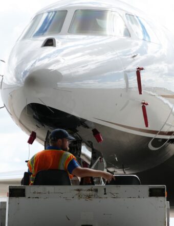 A worker in a high-visibility vest operates equipment near the nose of a parked airplane.