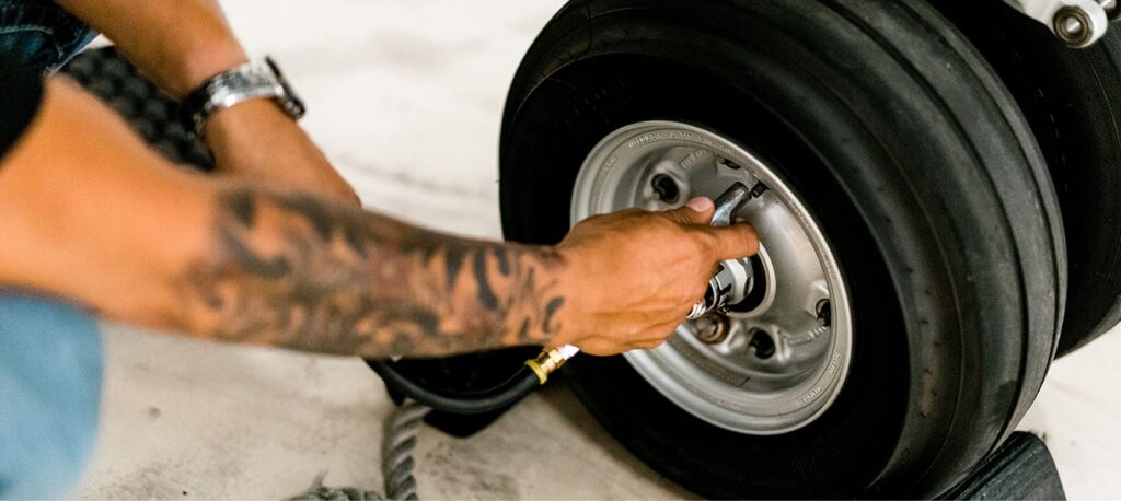 A person with a tattooed arm inflates a tire with a pump on a concrete floor.