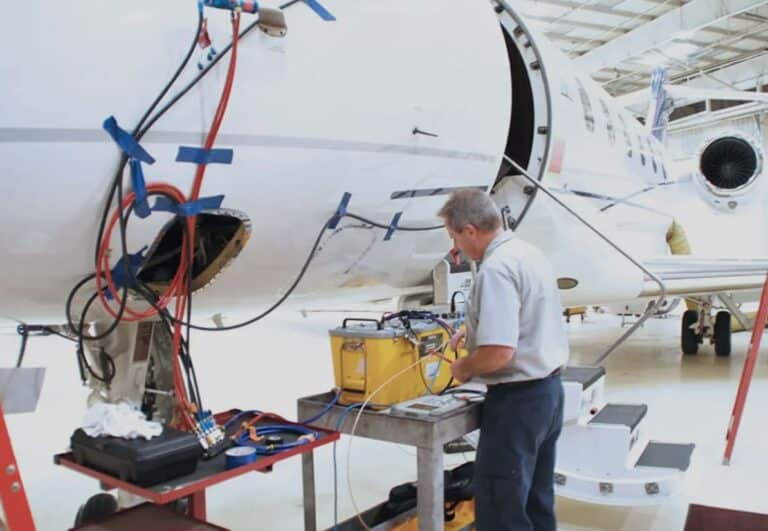 Technician working on airplane maintenance with tools and equipment in a hangar.